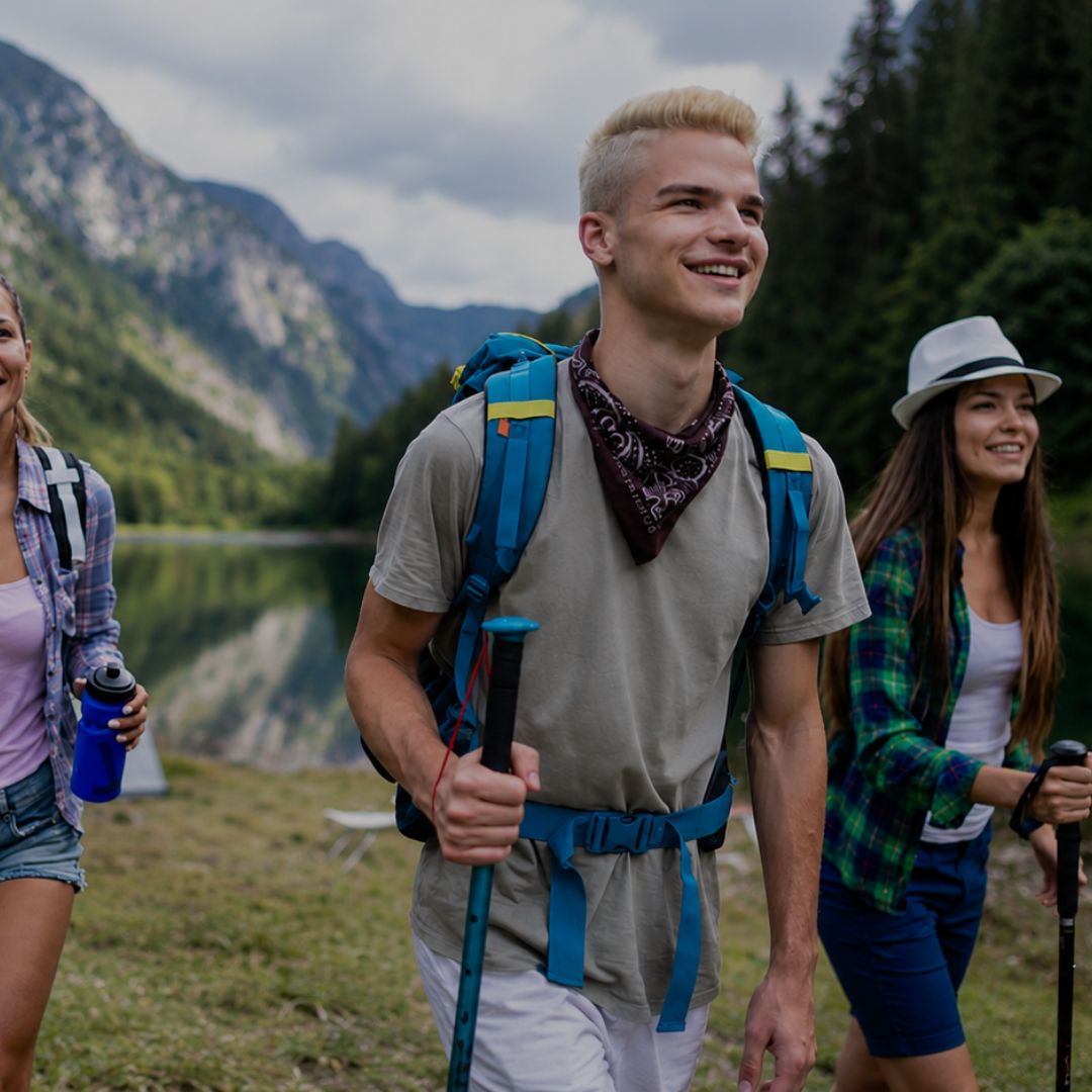 Three people hiking with backpacks and walking sticks in a mountainous area with a lake.