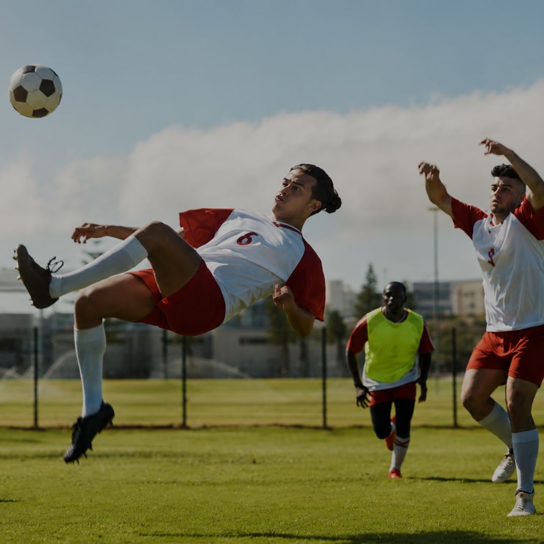 Soccer player in red and white uniform kicking a ball on a field with other players in the background.