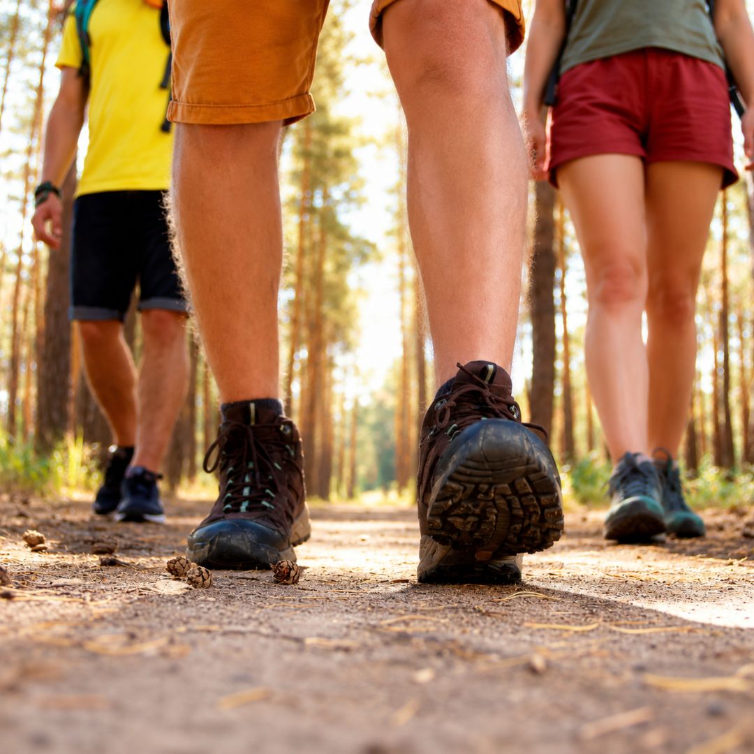 Three people hiking on a trail with focus on their feet wearing hiking boots.
