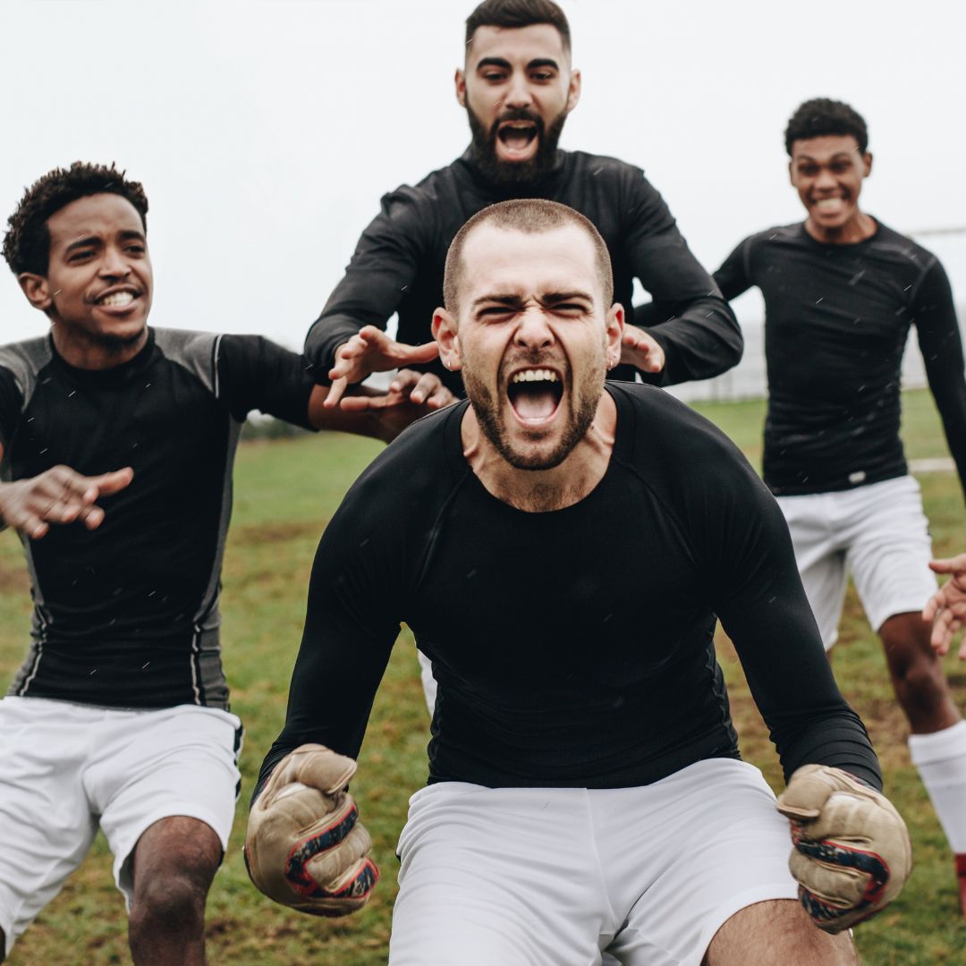 Four soccer players in black jerseys and white shorts on a grass field.